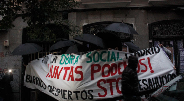 Activistas tapados con paraguas y una pancarta mientras abren la puerta del bloque en el número 33 de la calle Corredera Baja de San pablo, en Madrid.