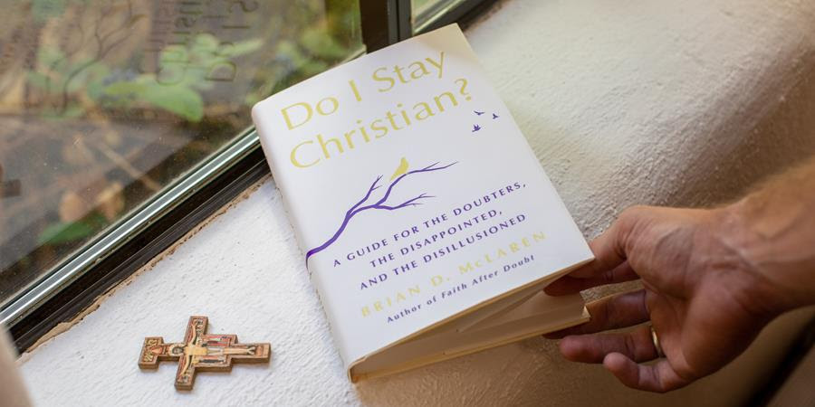 A photograph of the book Do I Stay Christian? sitting on a window sill while someone holds the book.