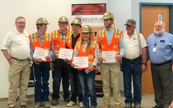Graduates don orange safety vests and gold hardhats as they hold their certificates next to three staff members from the Regional Training Center.