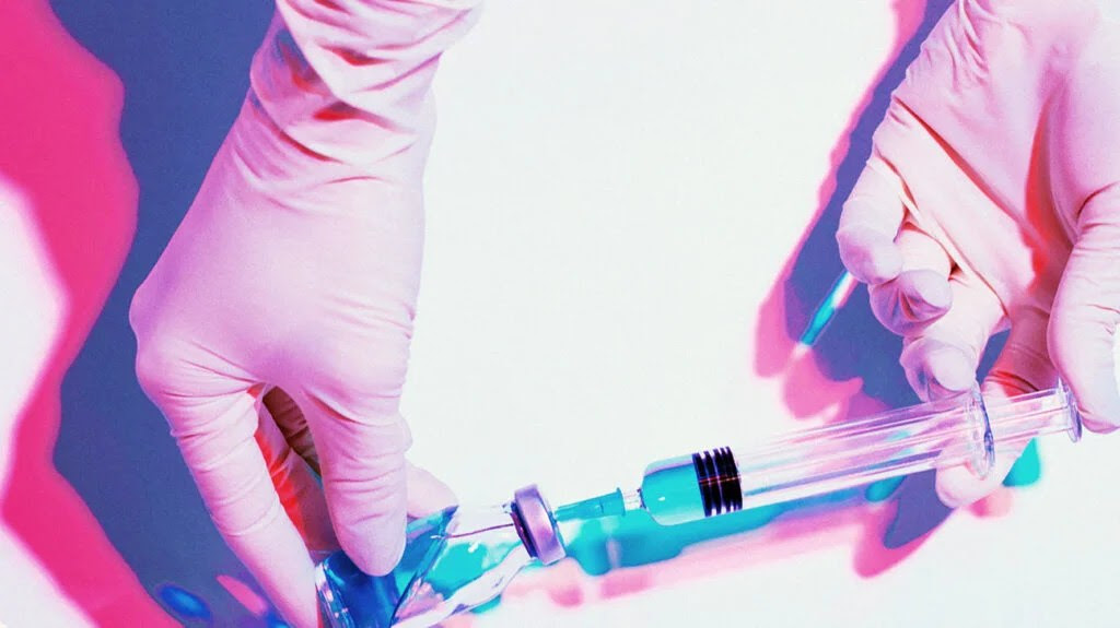 gloved hands holding syringe extracting vaccine dose from vial