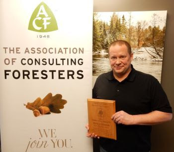 Brock VanOss, standing with a plaque in front of a sign, is the Michigan ACF 2023 Stewardship Forester of the Year. 