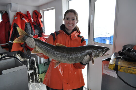 Woman in a bright orange coat holding a large trout