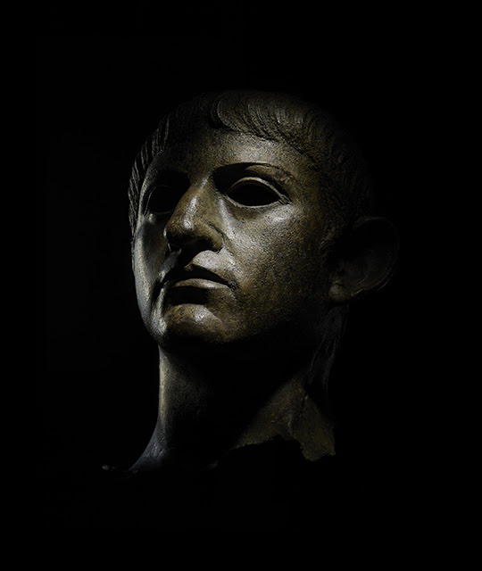 A bronze bust of the emperor Nero shown against a black background.