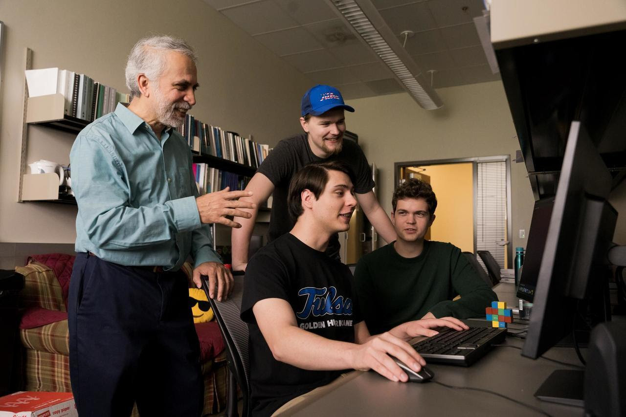 Professor guiding students on a computer.