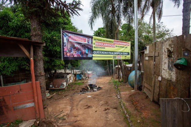 Cartaz a favor da regularização da ocupação dos Queixadas em Cajamar, alvo de processo de reintegração de posse e despejo, pendurada em uma rua de terra