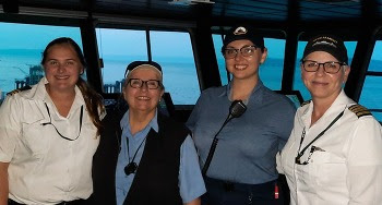Four people posing for a photo in the pilothouse of a ferry