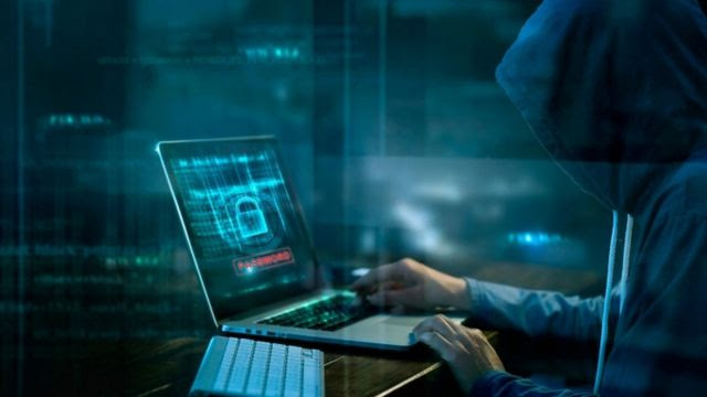 Pessoa encapuzada em ambiente escuro mexendo em computador