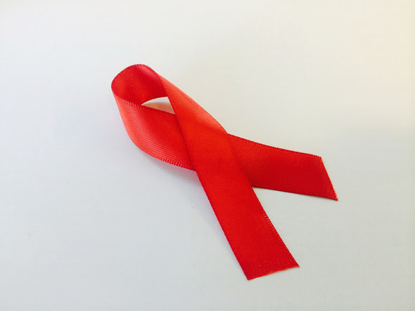 Red AIDS awareness ribbon resting on white surface