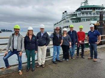 Eight people posing for a photo with a ferry in the background and the Seattle skyline far in the distance