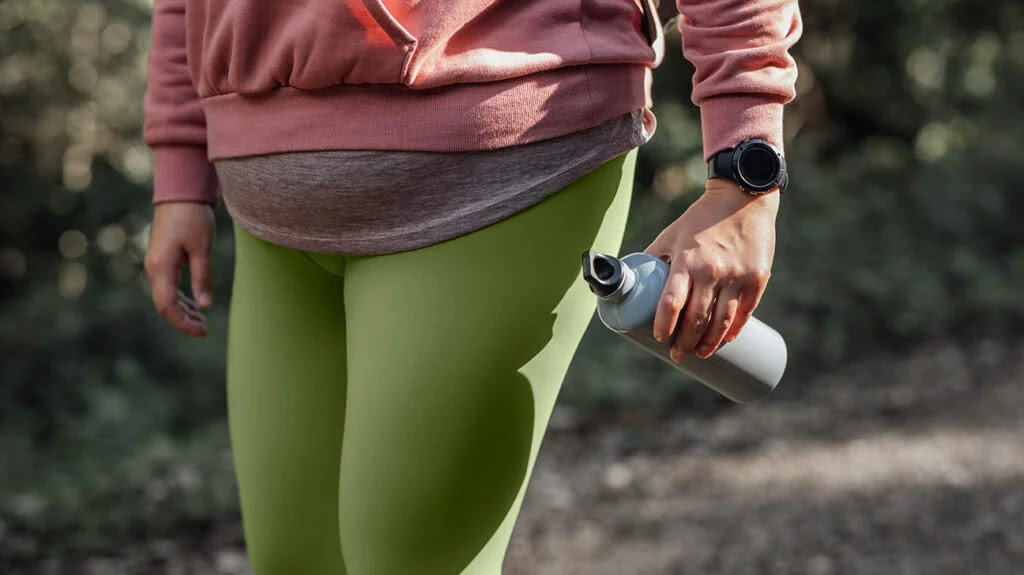 A close up of a woman running with a water bottle and smart watch