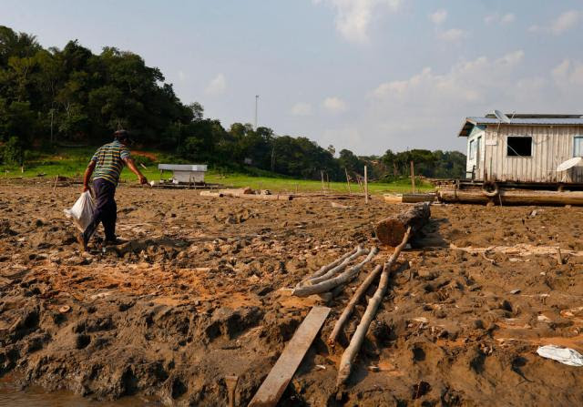 O pescador Chaberlan Pereira dos Santos carrega um saco com peixes em frente a casas flutuantes, em trecho do rio Solimes afetado pela seca