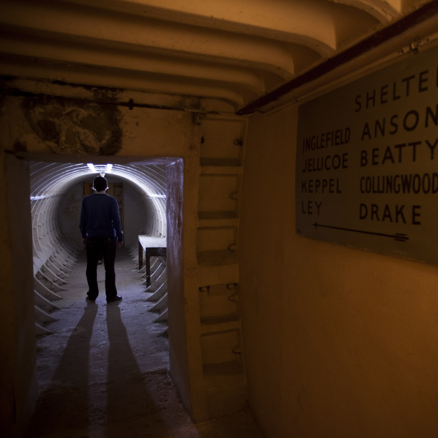 A person walks through a circular tunnel with a sign on the right hand side