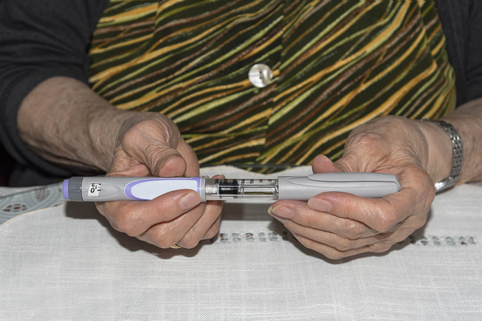 Close-Up Of Woman Holding Injection Pen At Table - stock photo