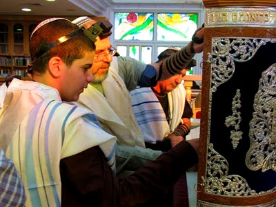 A Jewish 13-year-old male reads
from a Torah scroll protected by an elaborately
decorated Torah tik.