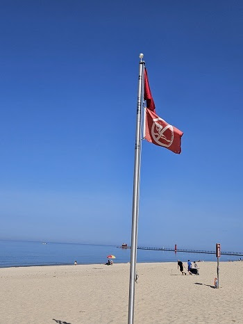 Two red flags hang from a tall pole on a sandy beach, near the shoreline. Double red flags on Great Lakes beaches mean don't go in the water.