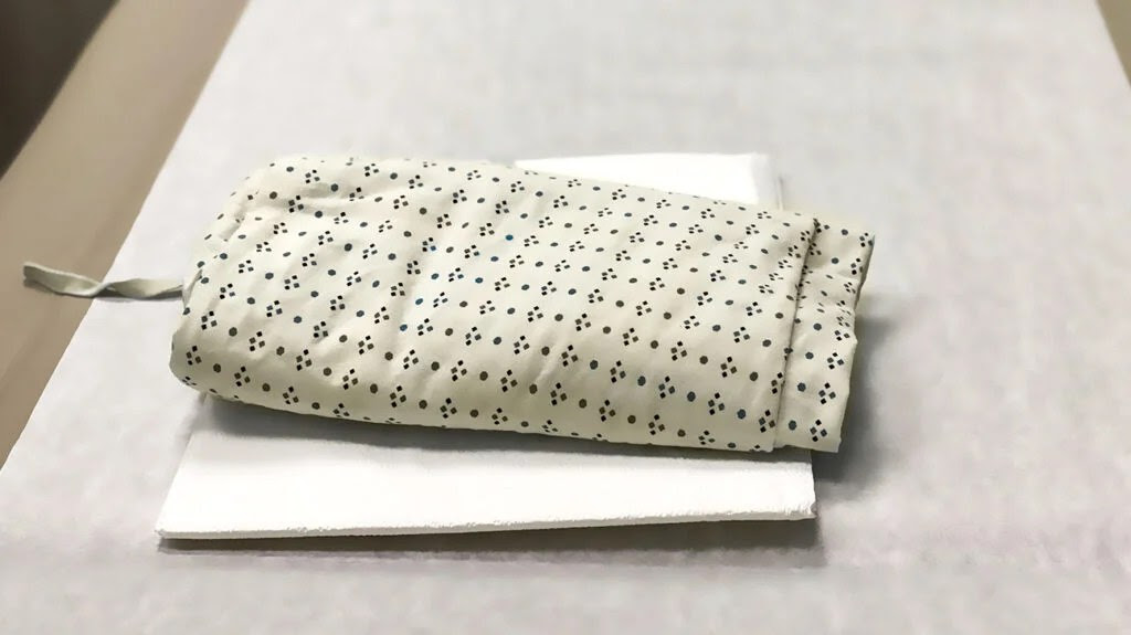 A folded hospital gown is placed on top of an envelope filled with documents