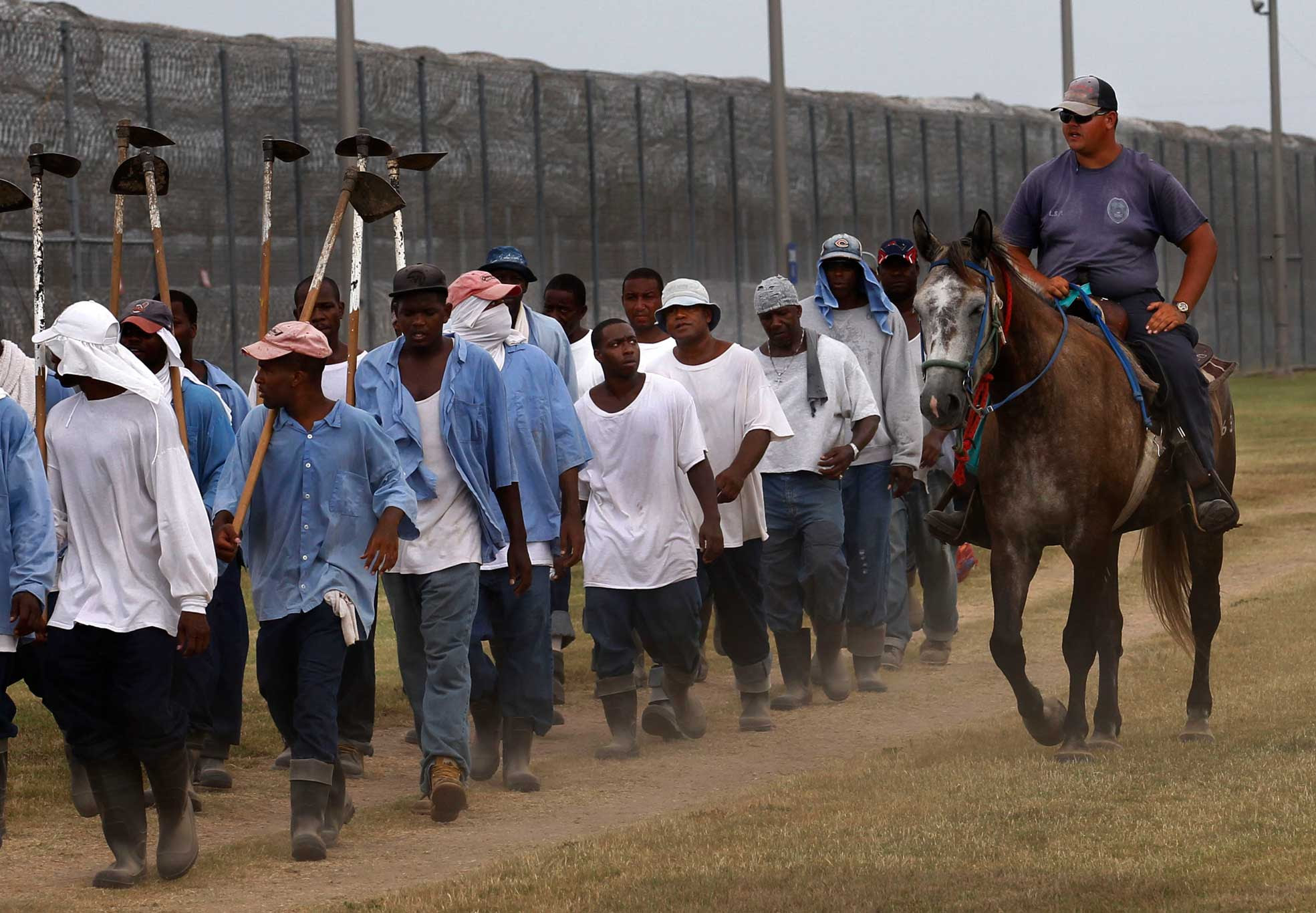 A prison guard oversees incarcerated people as they return to the dorms from farm work detail at the Louisiana State Penitentiary in Angola, La., on Aug. 18, 2011. The guard rides atop a horse that was broken in and trained by incarcerated people. (Image: AP Photo/Gerald Herbert)