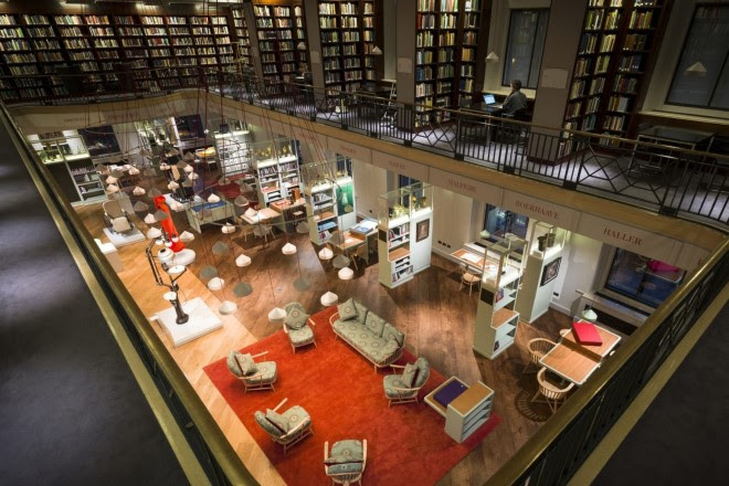 Photograph of the Wellcome Collection Reading Room from above, with a red carpet and green couch and chairs in centre frame, and book shelves in the background.