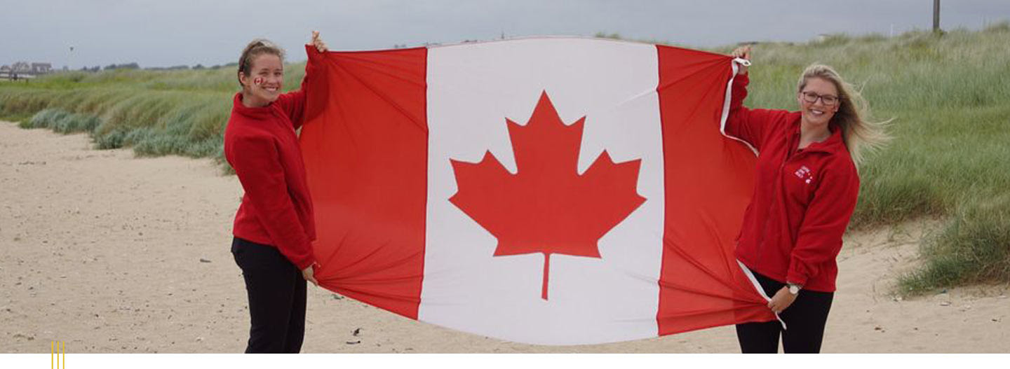 Image: Two women holding up a Canada flag on a beach.