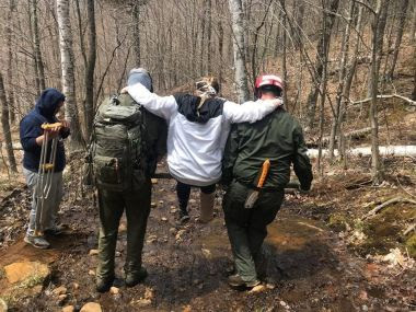 Two Forest Rangers carry a young woman with an injured leg through the woods on the trail