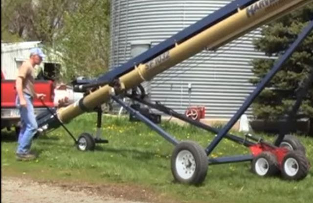 Man walks next to straight grain auger and moves it using the BackSaver 3 Straight Auger Mover. Grain bin and pickup truck are in background.