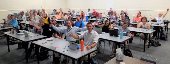 About 30 members of the standards review committee sit at classroom style tables with their arms raised in excitement to start their work on computer science standards.