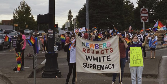 Multitud reunida en una intersección sosteniendo banderas del orgullo y carteles de Black Lives Matter