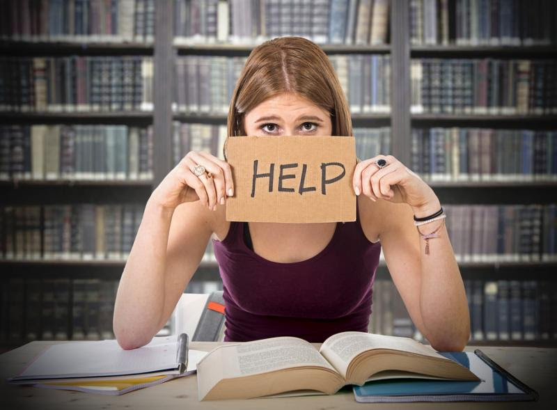 young beautiful college student girl studying for university exam in stress asking for help under test pressure sitting on desk with book in youth education concept