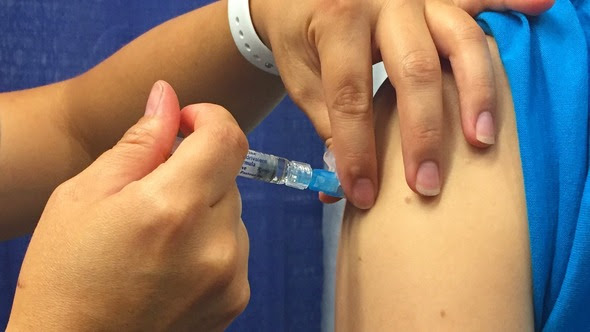 Hand injects vaccine through a syringe into a person’s shoulder muscle.