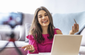 Foto de una mujer hispana sonriente y parlante sentada detrás de una computadora portátil