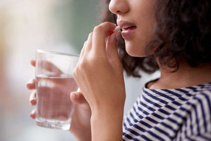 Cropped portrait of a woman taking her medication. She has a glass of water in one hand.