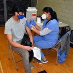 A student watches as a nurse gives him a vaccination shot in the shoulder during a COVID vaccination clinic at Edsel Ford High School in May 2021.