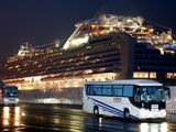 Buses carrying U.S. passengers who were aboard the quarantined cruise ship the Diamond Princess, seen in background, leaves Yokohama port, near Tokyo, early Monday, Feb. 17, 2020. The cruise ship was carrying nearly 3,500 passengers and crew members under quarantine. (Jun Hirata/Kyodo News via AP)