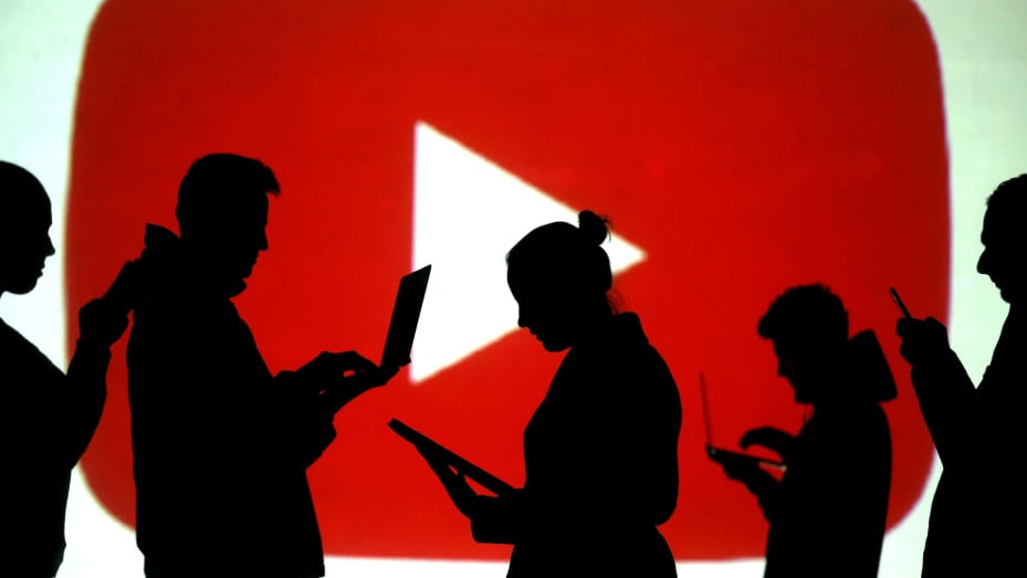 Silhouettes of laptop and mobile device users are seen next to a screen projection of the YouTube logo.