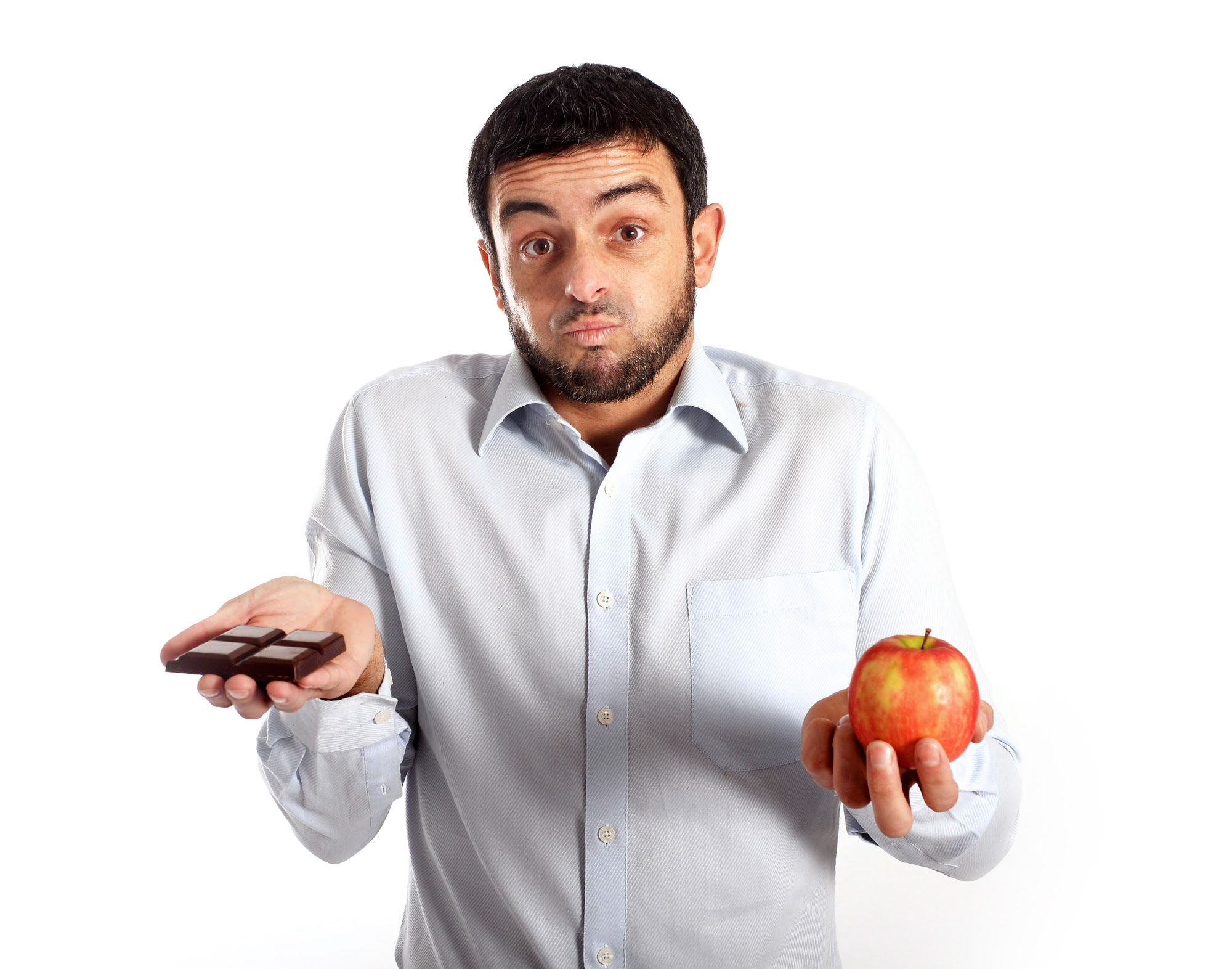 A man with a confused look on his face holding a chocolate in one hand and an apple in the other hand. 