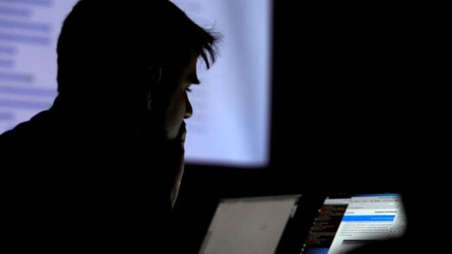 Homem em ambiente escuro olhando para tela de computador