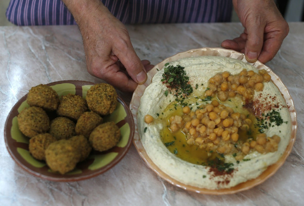 Palestinian restaurant owner Yasser Taha displays a plate of hummus, a paste made from chickpeas, and a bowel of falafel which are made from mashed and fried chickpeas