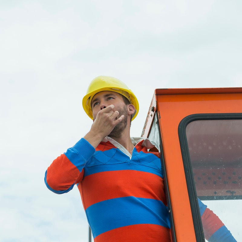 A construction workers holds his fingers in his mouth, about to whistle