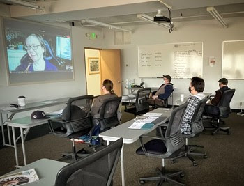 Photo of four people in a classroom looking at a person on screen