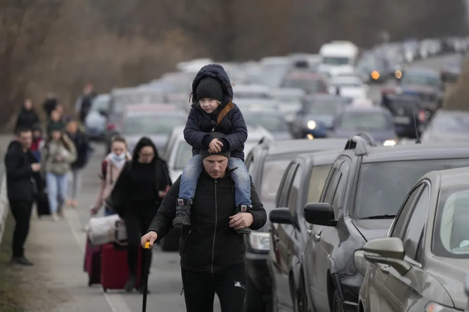 Ukrainian refugees walk alongside a line of vehicles.
