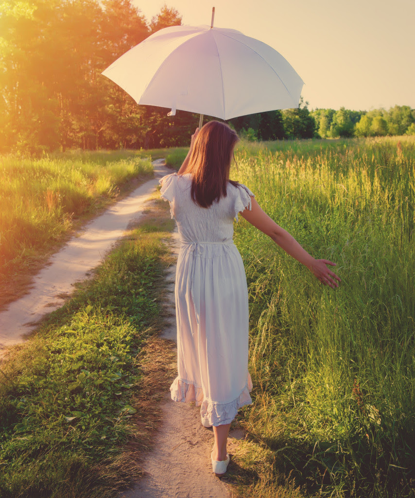 girl with an umbrella walking along a country road.