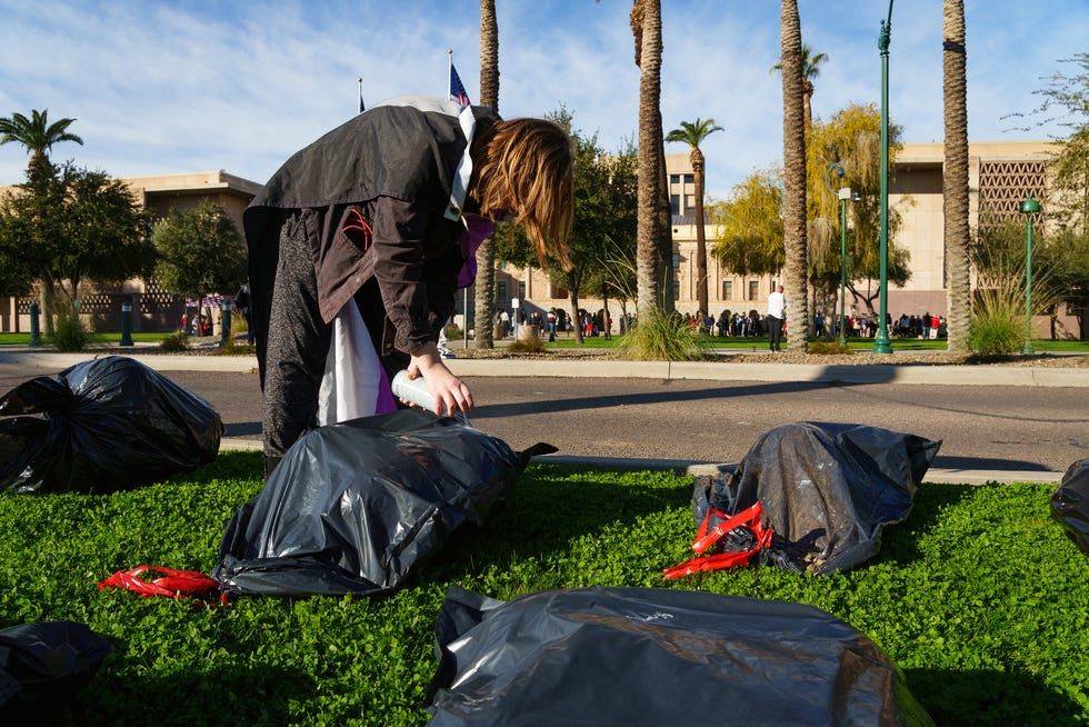 Corinne Collins spray paints messages on trash bags, meant to look like body bags, at the Wesley Bolin Memorial Plaza, across the street from the Arizona state Capitol, as part of a protest demonstration against anti-LGBTQ laws on Jan. 9, 2023, in Phoenix.