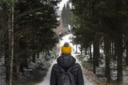 A woman hikes in the snowy woods wearing a yellow hat.