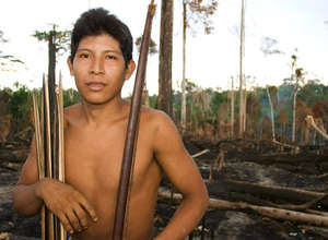 Un hombre awá entre los restos carbonizados de la selva de su tribu.