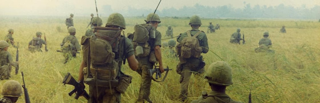 Color photograph of soldiers in the Vietnam War walking across a rice field