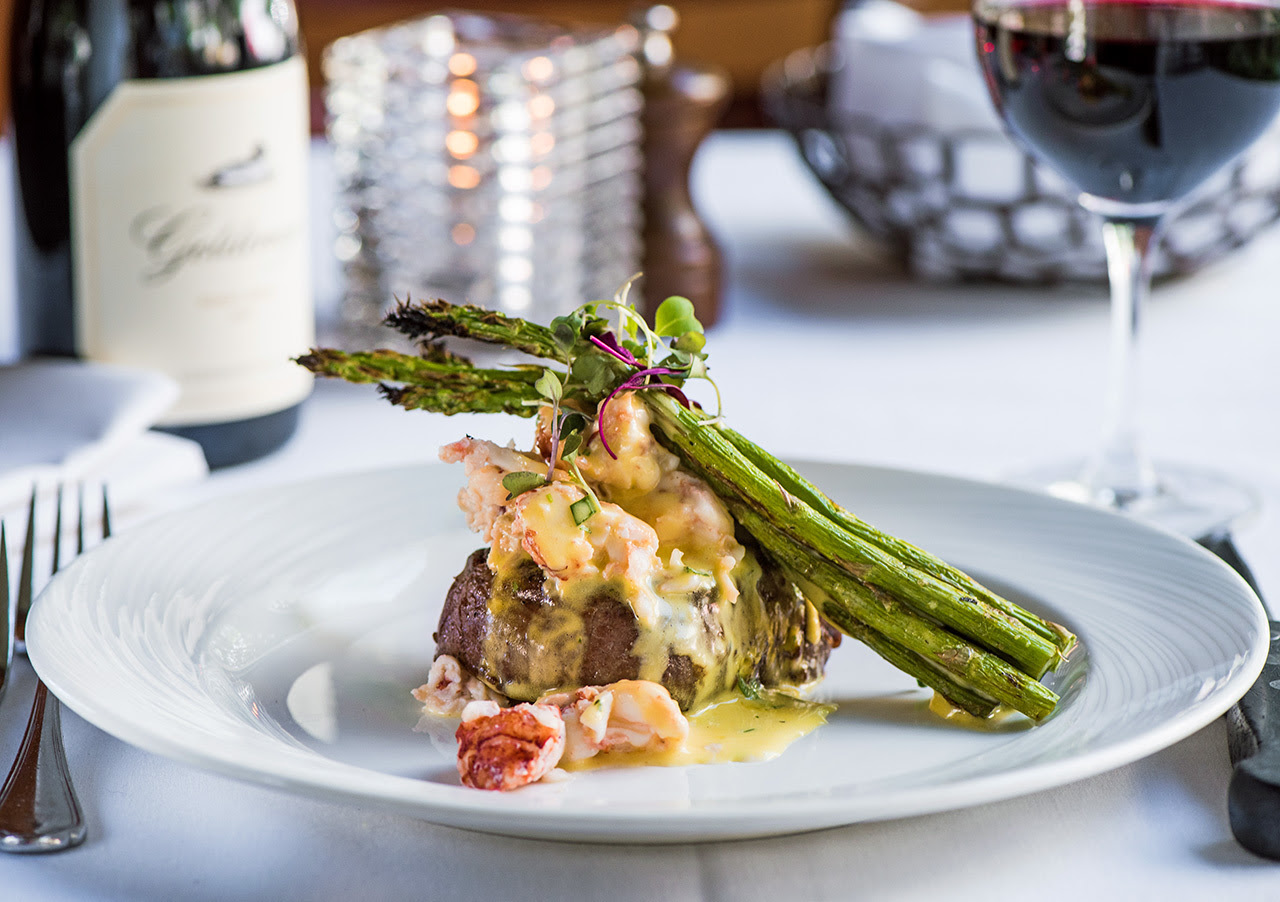 Filet Mignon topped with lobster and asparagus with red wine on a table
