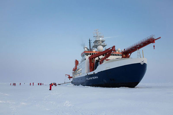 Researchers walk on an Arctic ice floe beneath the Polarstern ship