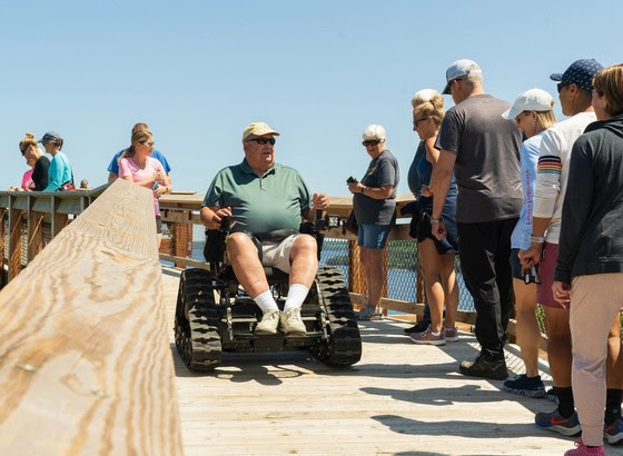 A man rides in an all-terrain wheelchair on Eagle Tower, surrounded by onlookers. 