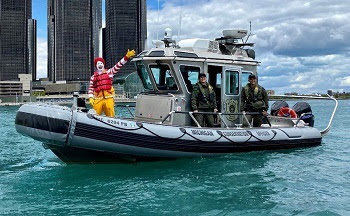 Ronald McDonald, waving, and DNR conservation officers, all wearing life jackets while on a patrol boat on the water
