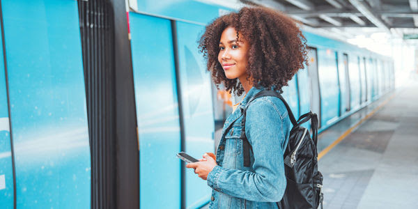 A young Black woman stands next to a train on a platform.